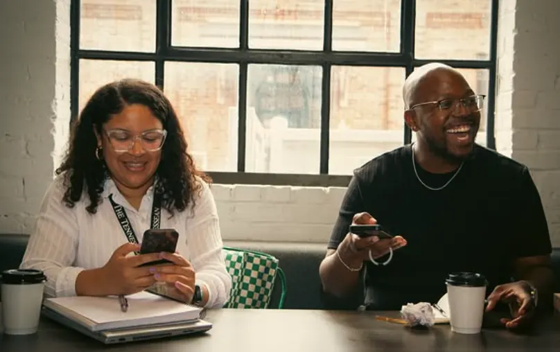 Two people laughing at a table with coffee cups